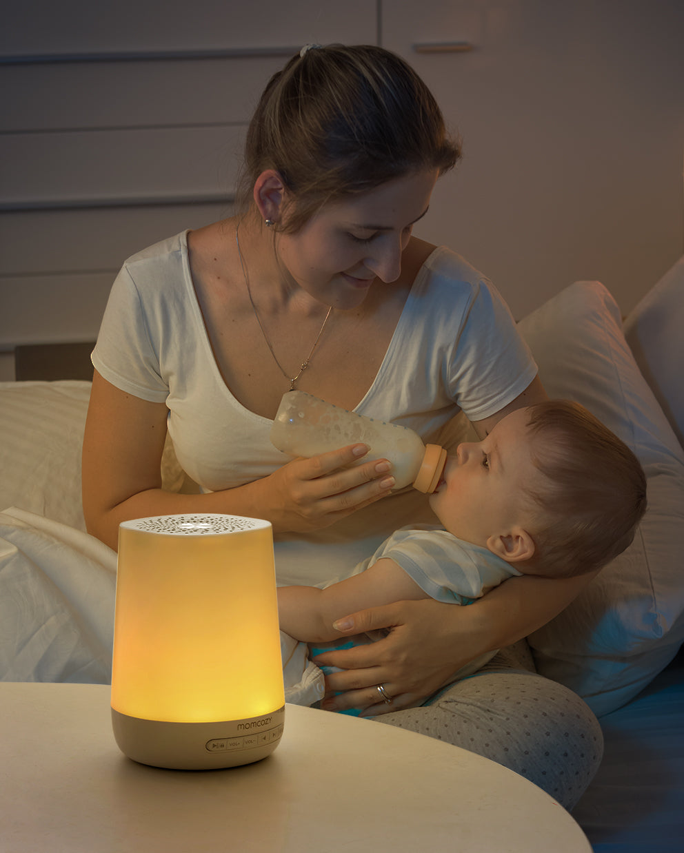 Momcozy Smart Baby Sound Machine with warm light, alongside mother feeding baby with bottle.
