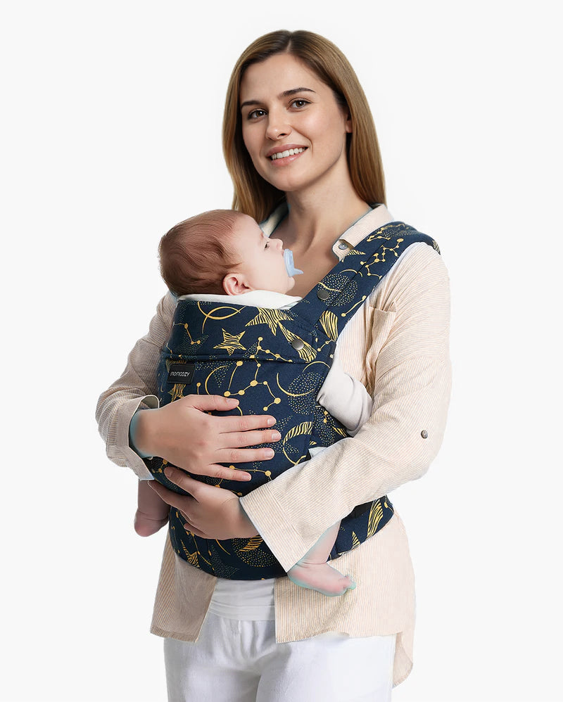 Momcozy PureHug navy baby carrier with star and constellation print, a woman smiles while holding her sleeping newborn.