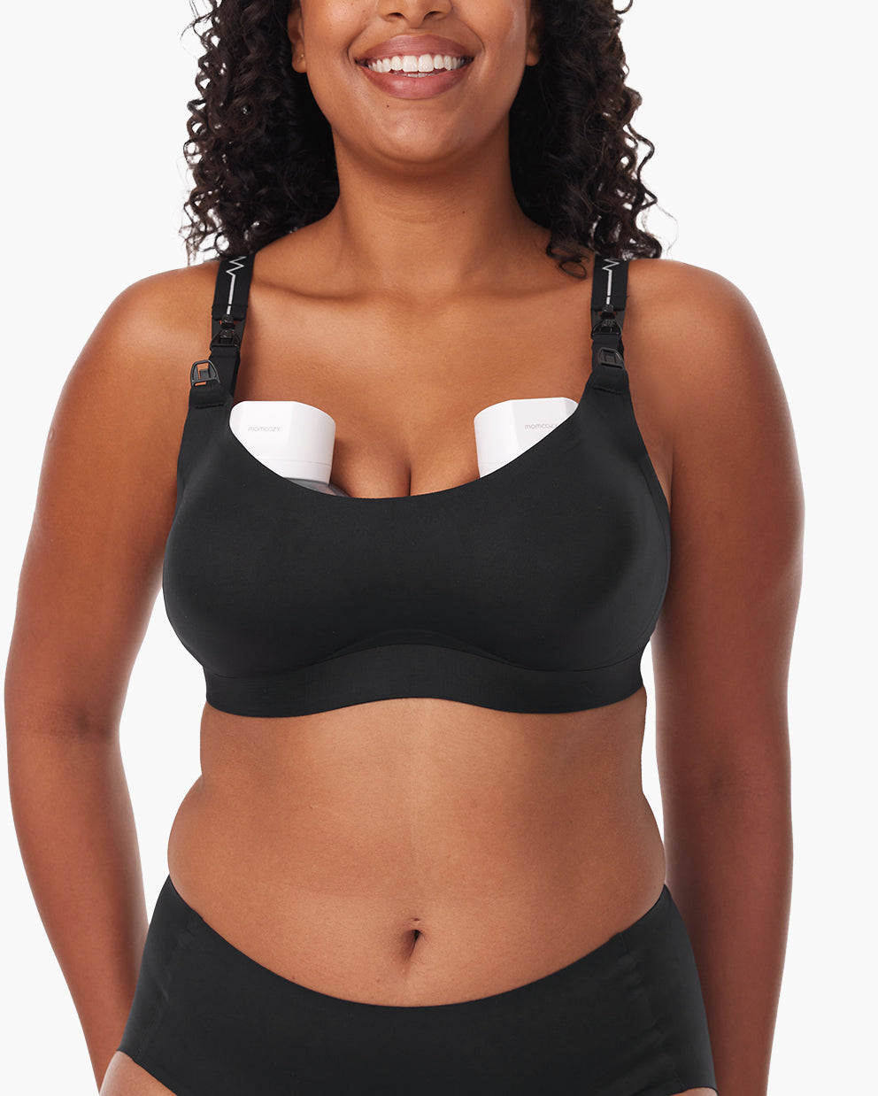 Smiling woman in black nursing and pumping bra with wearable breast pump, highlighting comfort and ease.