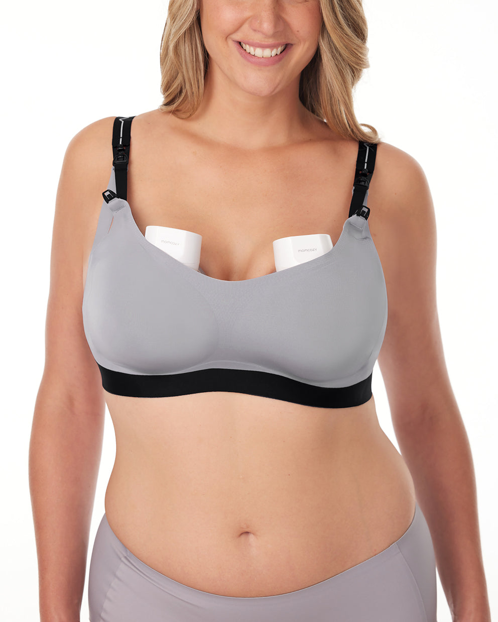 Smiling woman in gray nursing and pumping bra with removable straps, designed for wearable breast pumps.