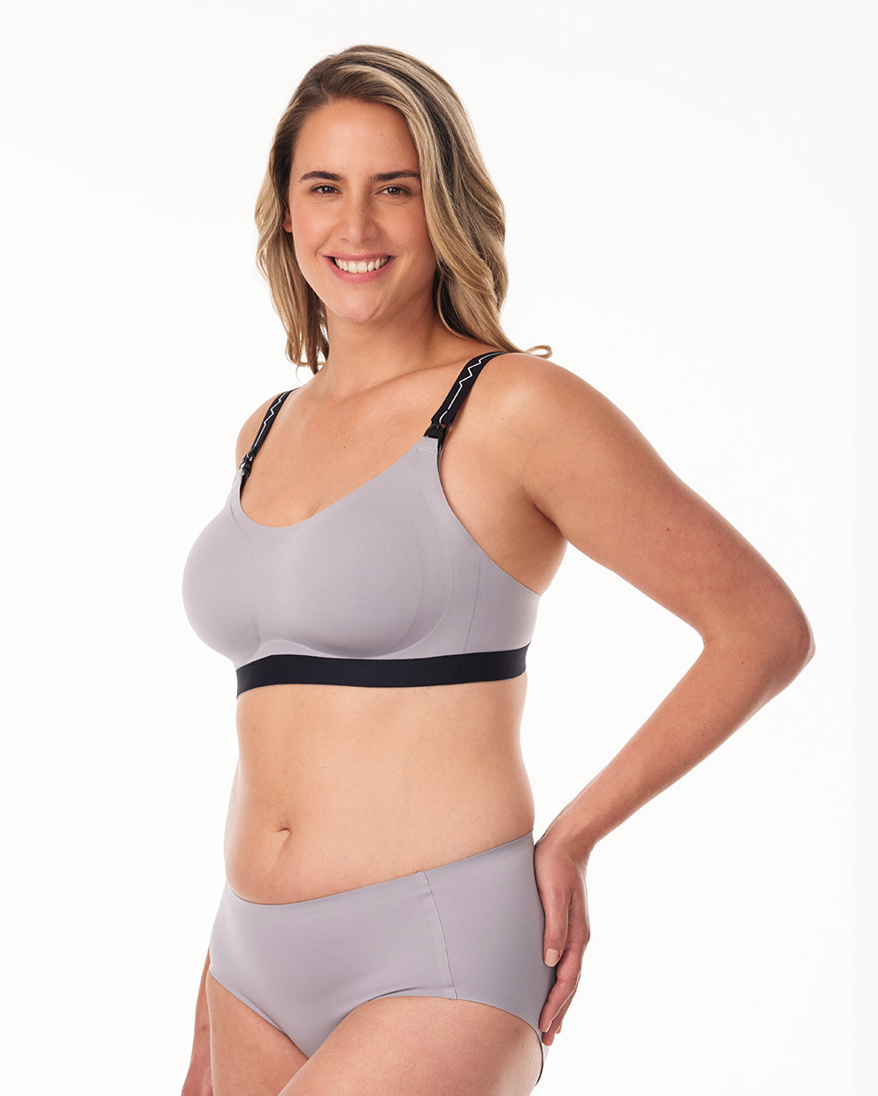 Smiling woman in gray nursing and pumping bra with removable straps, ideal for breastfeeding mothers.